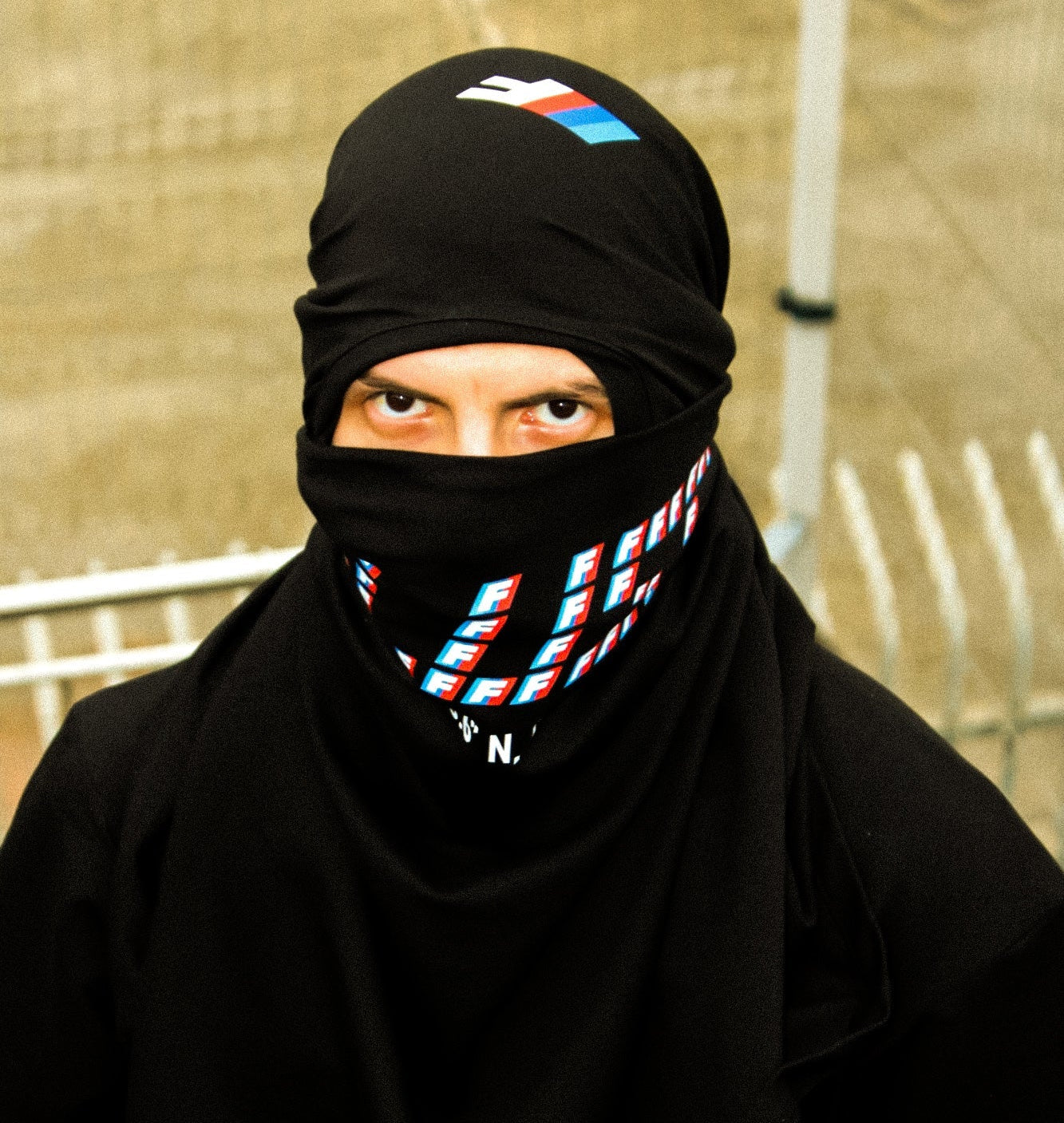 Person wearing a black Fluss Equipe  shirt with a logo print, standing against a neutral background.